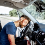 Bodily injury resulting from car accident.. Bloodied man unconscious in drivers seat with with head resting on steering wheel.